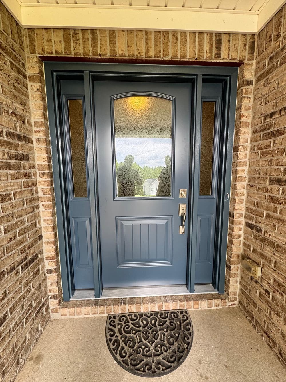 Navy blue entry door with half glass and sidelites in a brick entry
